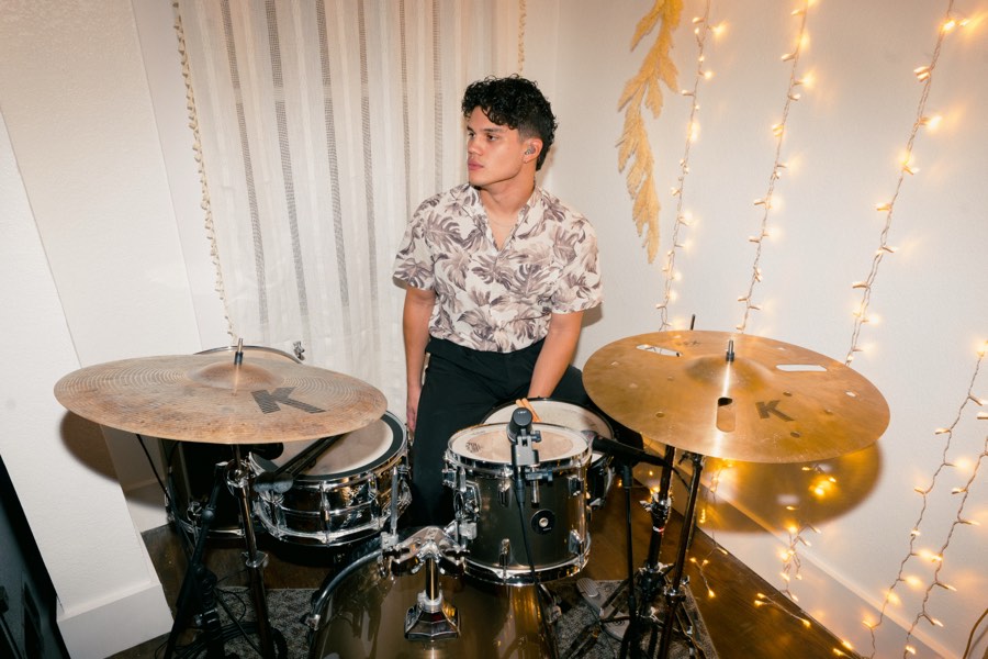 MAELO at a drum kit, string lights behind him